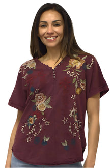  Woman wearing a burgundy shirt with floral embroidery on a plain background