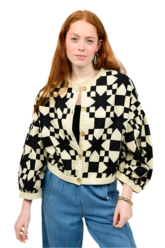 Person wearing a black and white patterned cardigan with blue jeans on a plain background