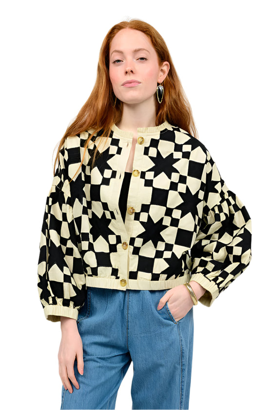 Woman wearing a black and white geometric patterned jacket with blue jeans on a white background