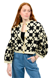  Person wearing a black and white geometric patterned jacket with blue jeans on a white background