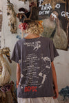 Person wearing a dark gray t-shirt with graphic designs and text, standing in a room with artistic decorations.