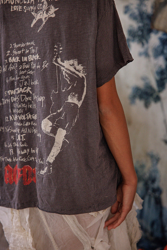 Person wearing a dark t-shirt with graphic design and text, standing against a blurred background.
