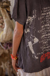 Person wearing a dark t-shirt with a graphic design and text, standing in a blurred indoor setting.