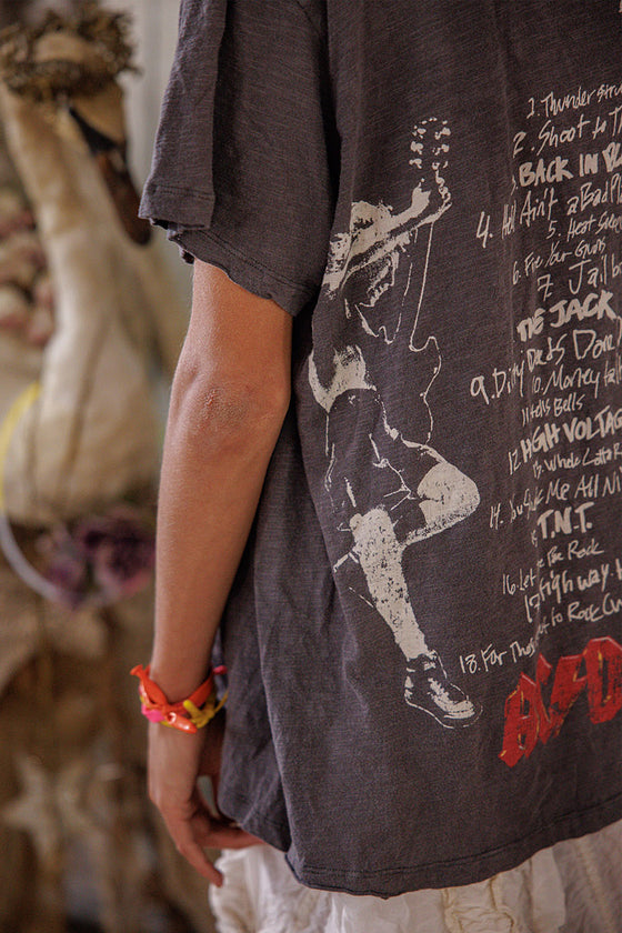 Person wearing a dark t-shirt with a graphic design and text, standing in a blurred indoor setting.