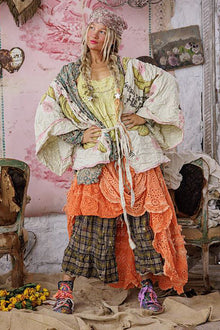  Person wearing a colorful, layered outfit in a rustic indoor setting with floral decorations.