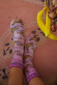  Purple socks with banana pattern worn by a person on a pink floor.