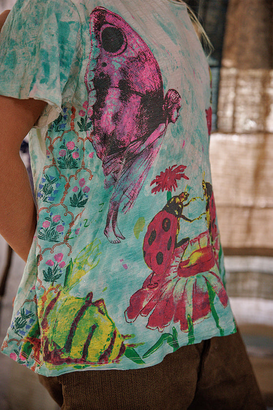 Person wearing a colorful shirt with floral and insect designs.