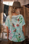 Person wearing a colorful t-shirt with butterfly designs and a cowboy hat indoors.