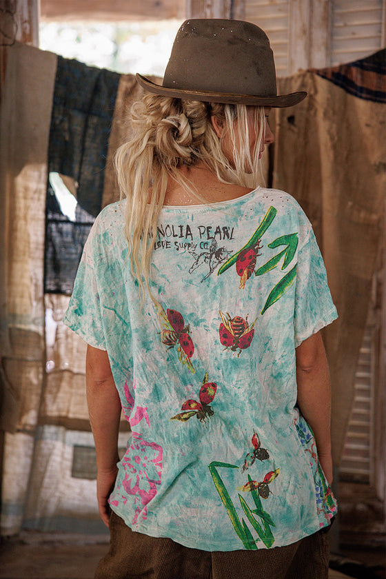 Person wearing a colorful t-shirt with butterfly designs and a cowboy hat indoors.