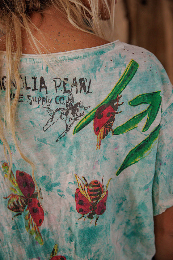 Person wearing a t-shirt with ladybug and leaf designs and 'Lilia Pearl' branding.