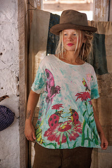  Woman wearing a colorful floral t-shirt and brown hat indoors.