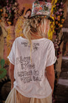 Person wearing a white t-shirt with text and a floral cap in front of a colorful mural.