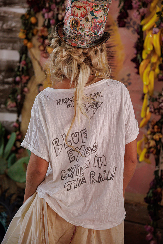Person wearing a white t-shirt with text, standing in front of floral decorations.