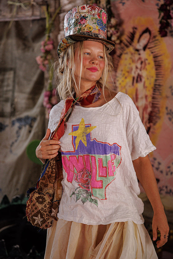 Young girl wearing a colorful top hat and graphic t-shirt with a patterned bag.