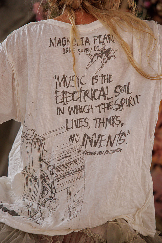 White t-shirt with black text and piano graphic on the back, worn by a person.