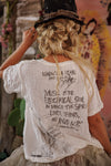 Person wearing a white t-shirt with text and graphics, sitting against a colorful wall.
