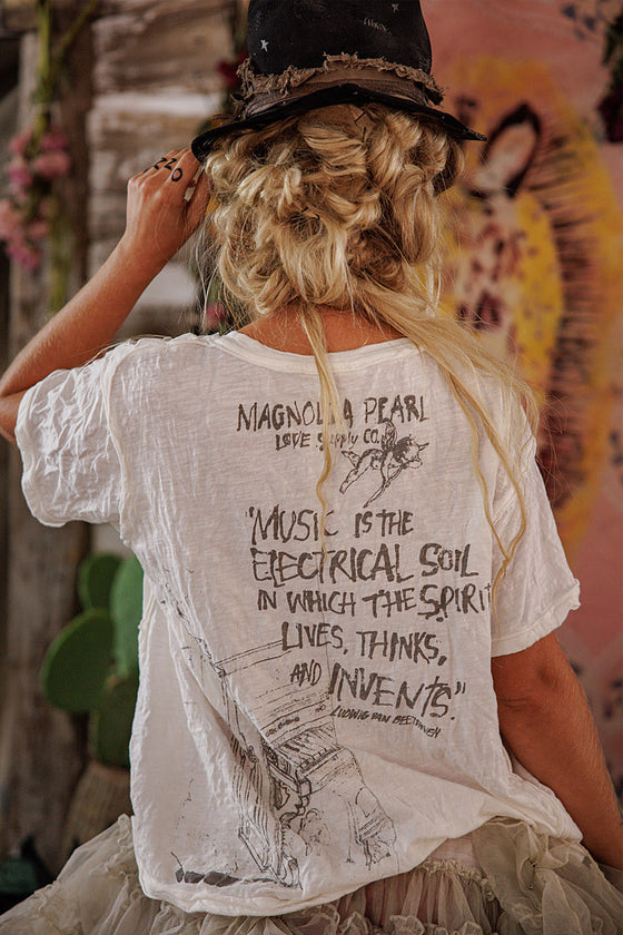 Person wearing a white t-shirt with text and graphics, sitting against a colorful wall.