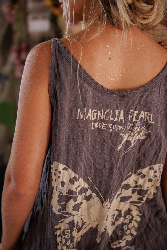 Person wearing a tank top with 'Magnolia Pearl' branding and butterfly design.