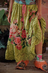 Person wearing a colorful skirt with floral patterns and bright orange shoes on a wooden floor.