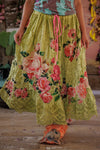 Person wearing a floral skirt with pink roses on a wooden floor.