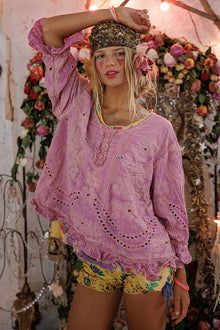  Woman wearing a pink embroidered top and colorful shorts in a decorated indoor setting.