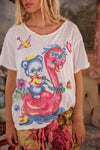 Person wearing a white t-shirt with a colorful graphic design of a bear and flamingo.
