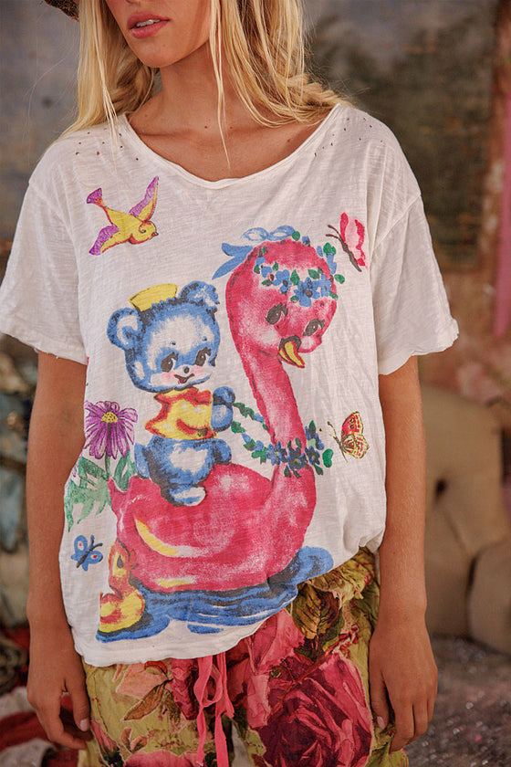 Person wearing a white t-shirt with a colorful graphic design of a bear and flamingo.