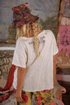 Person wearing a white t-shirt with text and colorful pants in a rustic setting