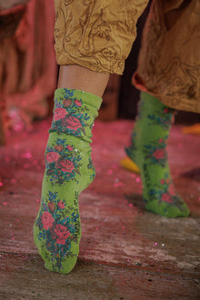  Green floral-patterned socks worn by a person on a wooden floor.