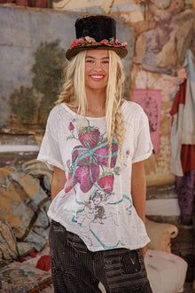  Woman wearing a white t-shirt with colorful graphics and a black top hat in an artistic setting.