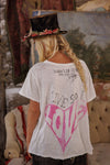 Person wearing a white t-shirt with text and graphics, standing in a rustic indoor setting.