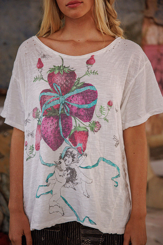 White t-shirt with a colorful design featuring strawberries and a bow, worn by a person.
