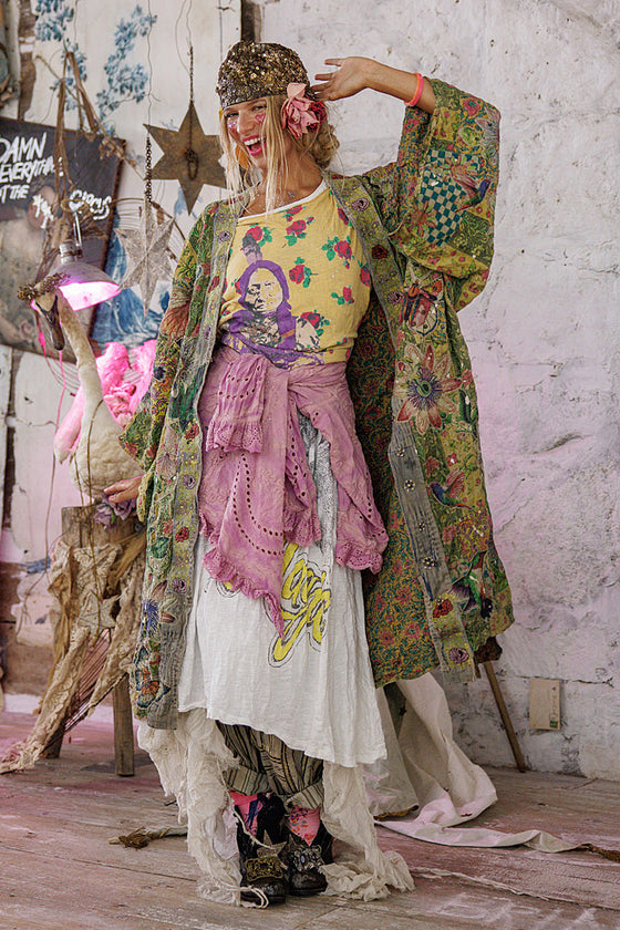 Person wearing a colorful outfit with a floral headband and scarf, standing in a room with decorative elements.