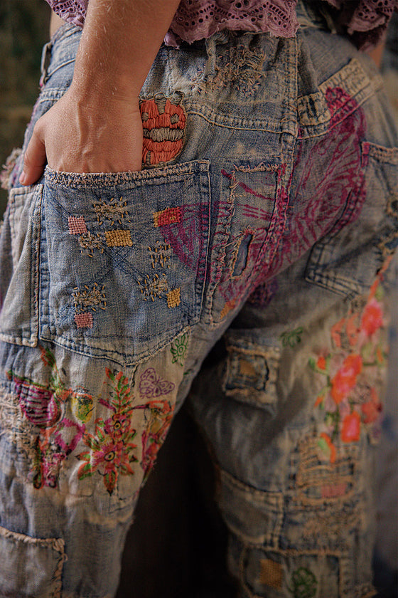 Close-up of a person wearing a patchwork denim jacket with colorful embroidery.