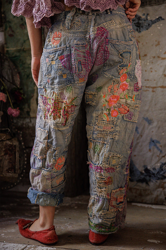 Person wearing patchwork pants with floral patterns in a rustic setting
