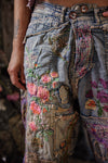 Close-up of denim pants with floral embroidery and patches.