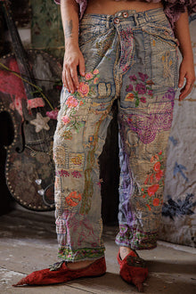  Person wearing patchwork jeans with floral patterns in a rustic setting.