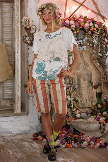  Woman in a floral dress and striped shorts standing in a decorated room with flowers and vintage items.