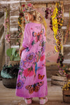 Woman wearing a pink dress with butterfly designs in a rustic setting.