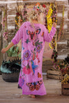 Woman wearing a pink floral and butterfly patterned dress in a rustic setting with hanging flowers.