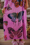 Person wearing a pink dress with butterfly designs on a wooden floor.