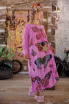 Woman in a pink dress with butterfly patterns standing in a rustic setting.