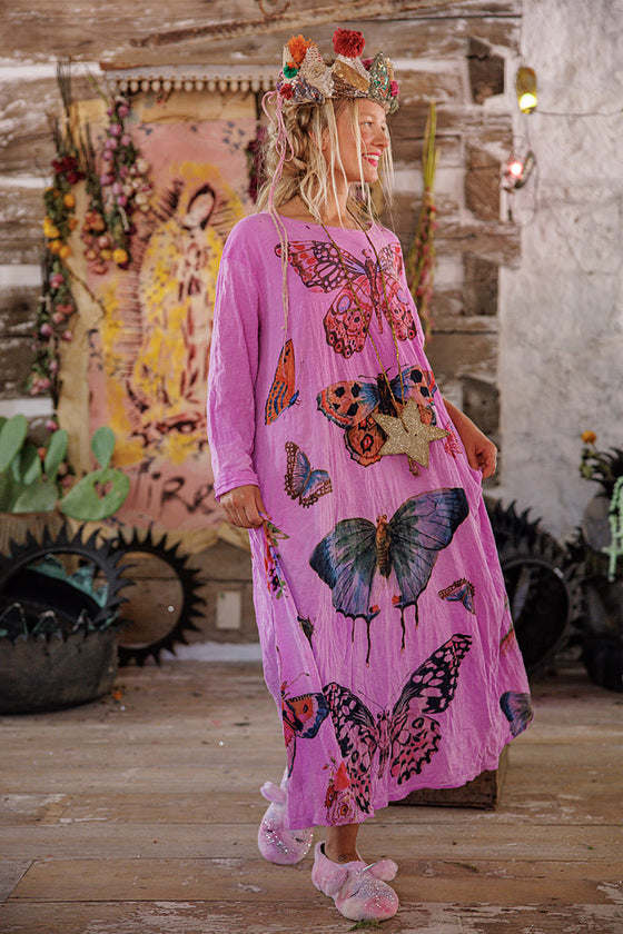Woman in a pink dress with butterfly patterns standing in a rustic setting.