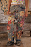 Person wearing patchwork jeans with floral and abstract designs in a rustic setting.