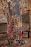 Denim pants with colorful animal and floral embroidery in a rustic setting.