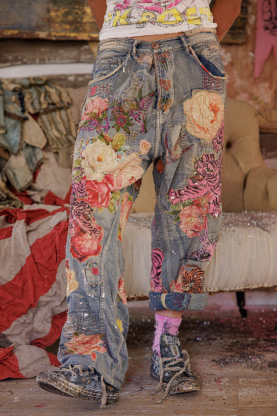 Person wearing floral patchwork jeans in a room with furniture and decor.