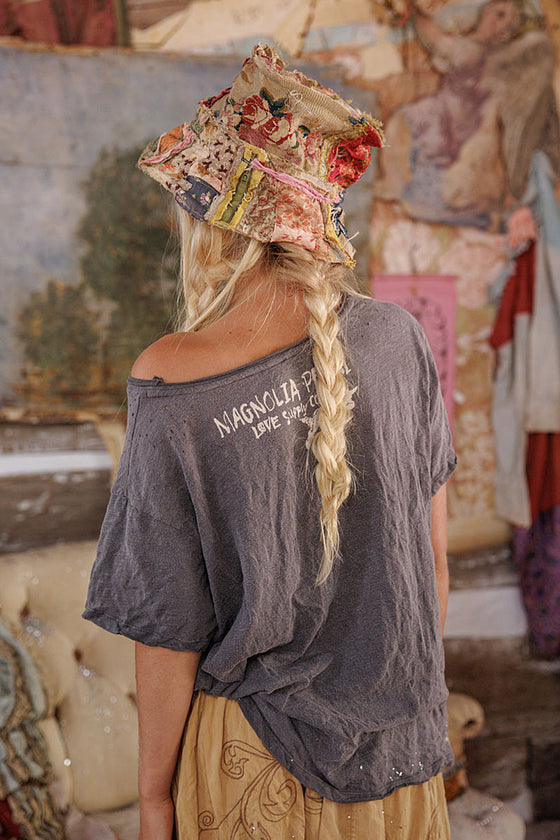 Person wearing a colorful hat and gray 'Magnolia' shirt in an art gallery setting