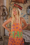 Woman wearing an orange dress with green and purple designs in a rustic room.