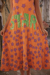 Orange dress with purple star patterns and green text held by a person.