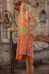 Woman in an orange dress with colorful text and patterns standing in a rustic bedroom.
